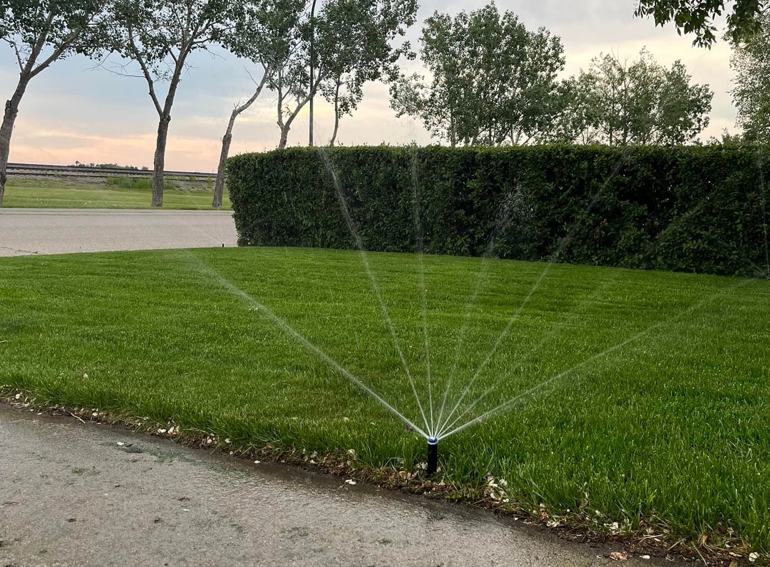 A detailed, photorealistic image of a diverse team of irrigation experts discussing plans over blueprints in front of a variety of properties, from a charming house to a large commercial landscape, illustrating collaboration and diversity in irrigation solutions.